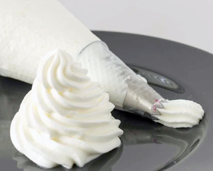 Spiral of whipped cream next to a piping bag on a plate