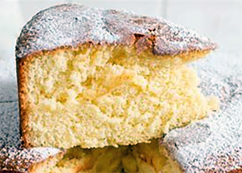 slice of almond sponge cake dusted with icing sugar set on top of the main cake
