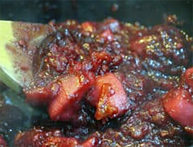 apple and tamarillo compote stirred with a wooden spoon