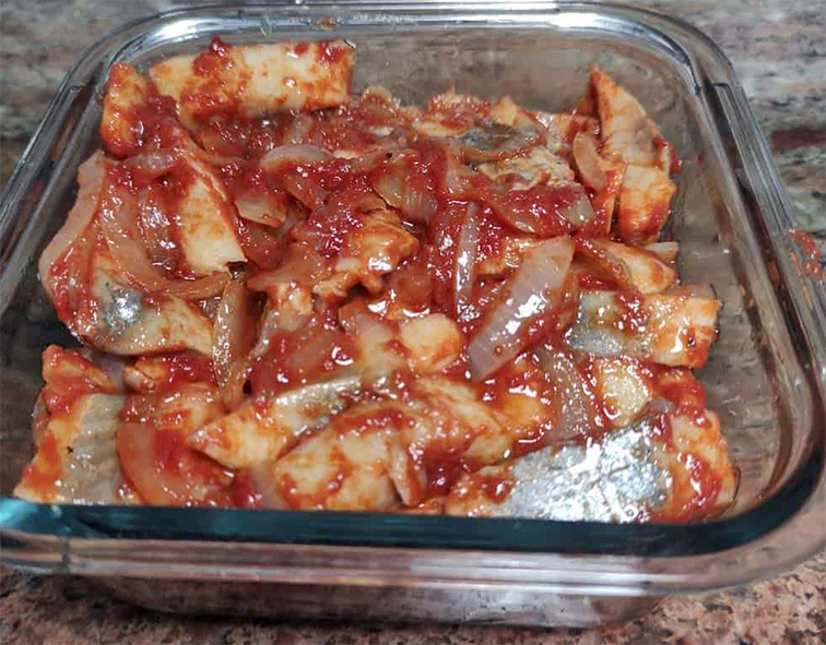 herring pieces with tomatoes and onions arranged in a glass baking dish prior to baking