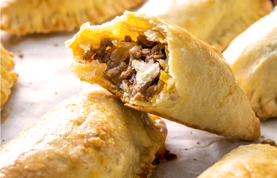 baked spicy beef and cheese empanada with one halved empanada leaning on another to reveal the filling