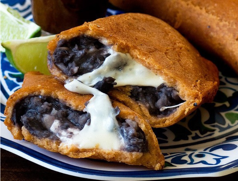 black bean and cheese empanada with maize dough split open to reveal the filling
