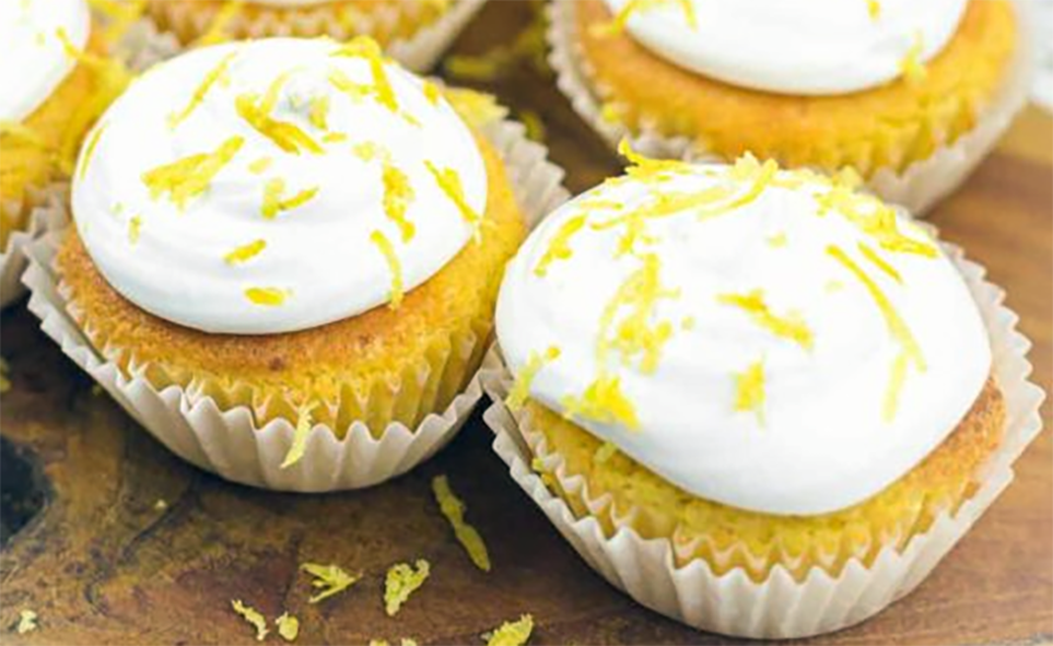 frosted citrus cupcakes in paper cases on a wooden chopping board