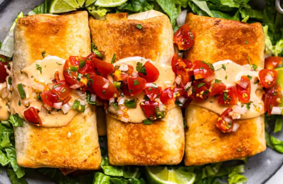 three baked chicken chimichangas on a bed of lettuce with a garnish of sour cream and salsa