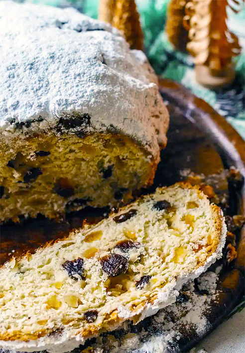 German Christmas bread loaf dusted with icing sugar and with one slice cut off and presented in front