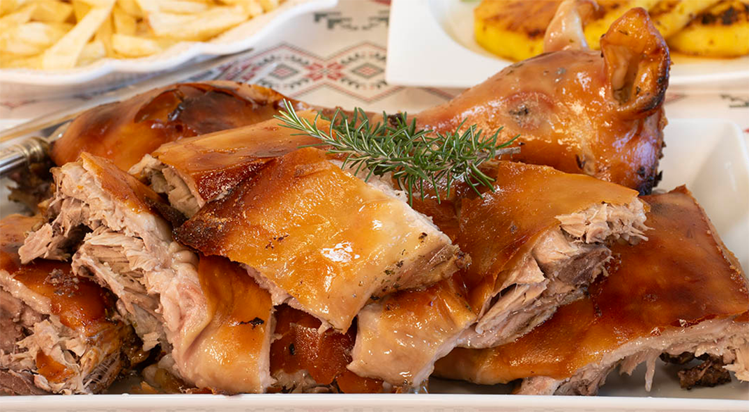 Cochinillo, pieces of baked suckling pig arranged in a serving dish and topped with a sprig of rosemary