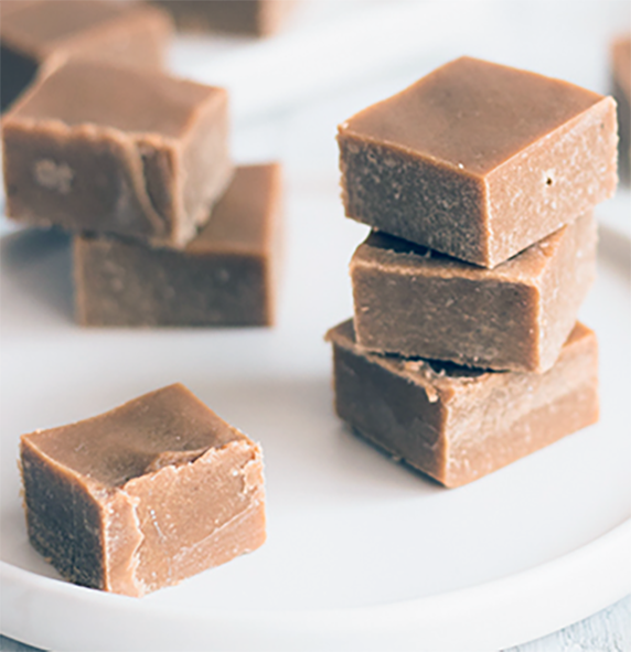 squares of coconut caramel fudge with wild flour arranged in stacks on a white plate