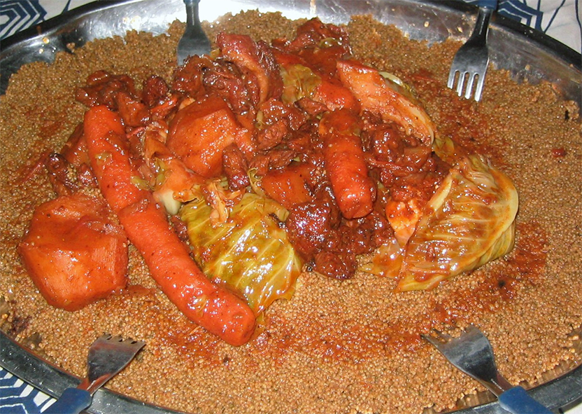 Dark Mauritanian couscous topped with mixed vegetables and camel meat in a tomato sauce