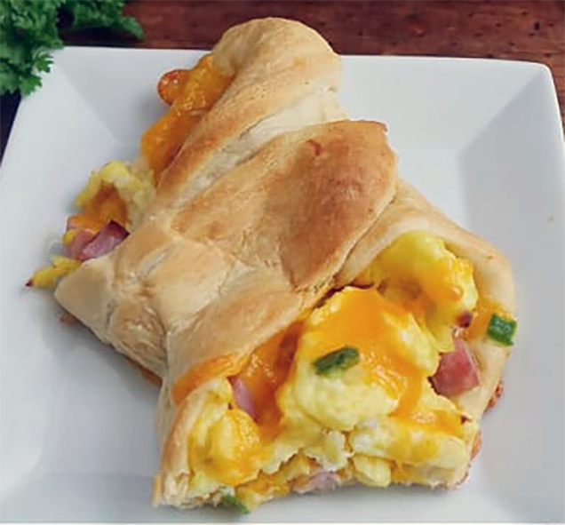 Crescent roll dough stuffed with soft-boiled eggs, ham, herbs and onion with three-cheese ranch dressing on a white plate