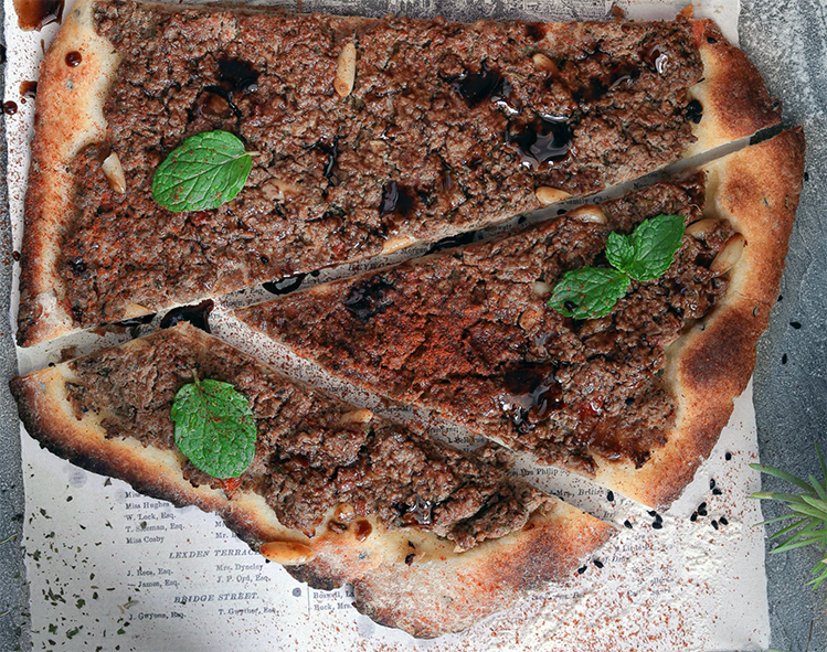 baked flatbread topped with meat, cut into pieces and garnished with fresh mint leaves