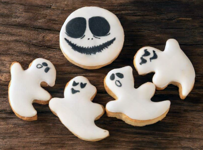 five ghost-decorated ginger biscuits on a wooden board