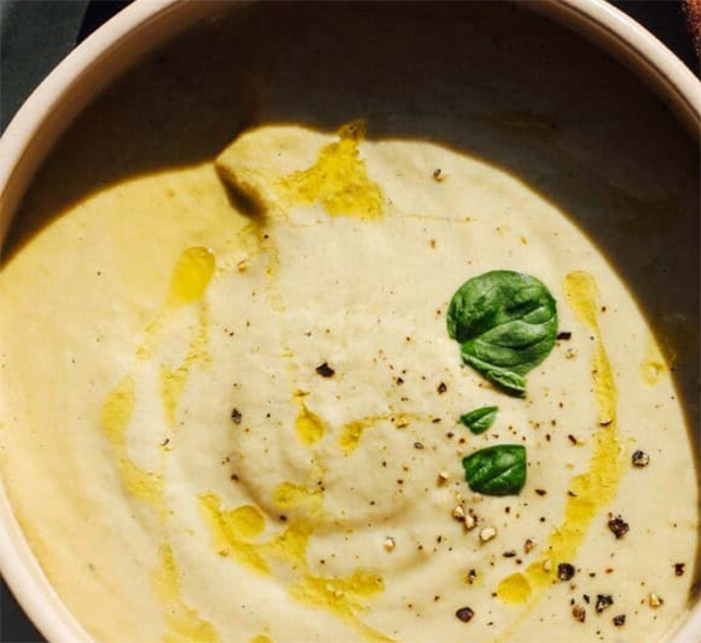 thick and creamy green tomato and potato soup in a deep bowl with a garnish of olive oil and basil leaves