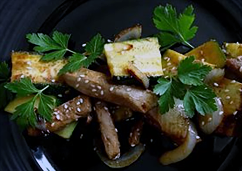 marinated tuna strips with onion and courgettes on a black plate with parsley