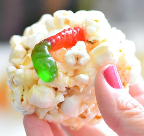 ball of popcorn bound with marshmallows with a gummy work emerging