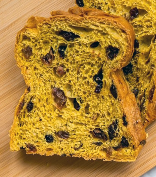 slice of fruited saffron cake on a wooden chopping board