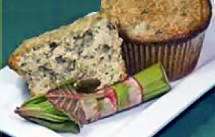 One whole and one half japanese knotweed muffins on a rectangular plate with the tip of a Japanese knotweed shoot
