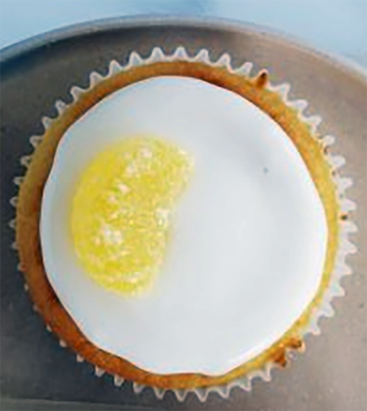 lemon yoghurt cupcake in a paper case served topped with white icing and candied lemon