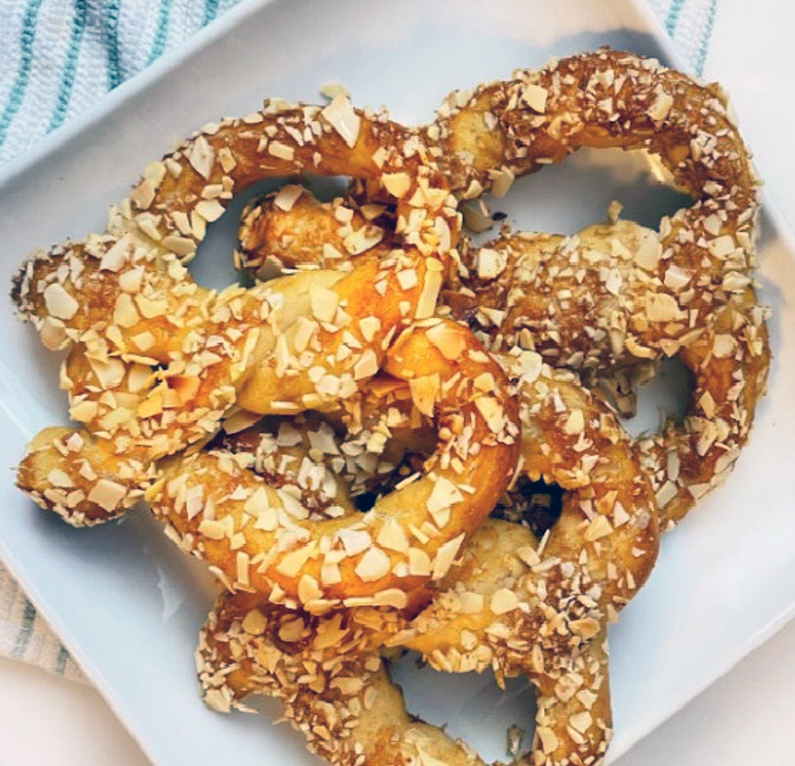 three almond pretzels decorated with almonds piled on a pale