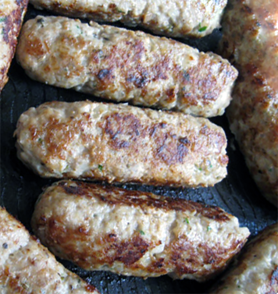 skinless pork and sage sausages cooking in a frying pan