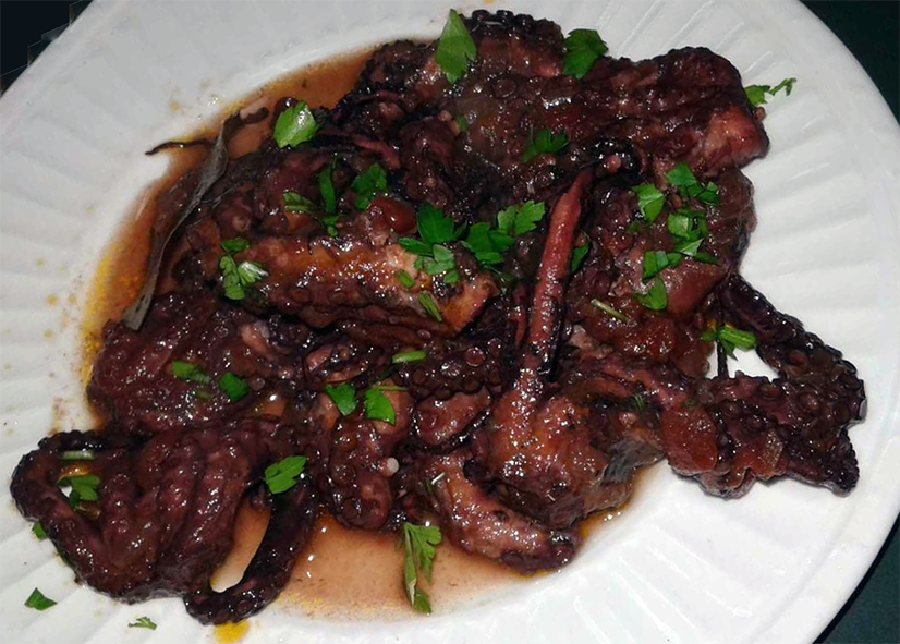 octopus in wine sauce served on a white plate garnished with spring onion greens