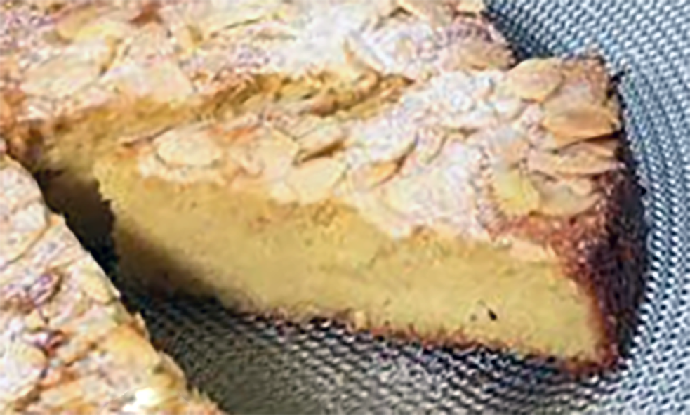 wedge of pounded almond cake on a plate garnished with powdered sugar and slivered almonds