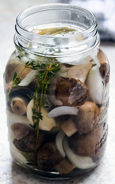 pickled baby filed mushrooms in a jar with springs of thyme