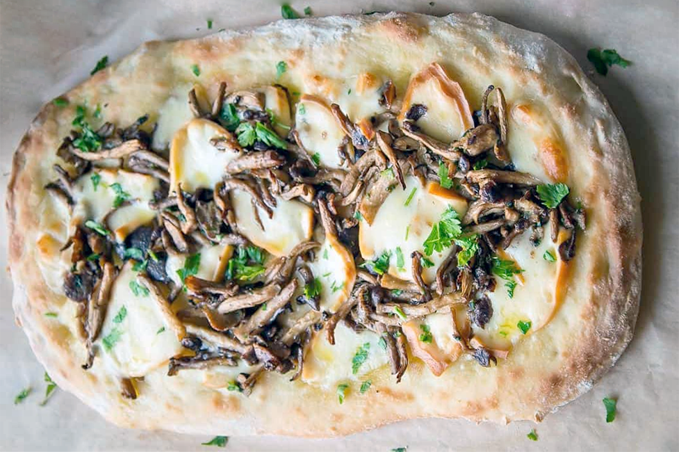 oval pinsa romana pizza on a marble work top with mushroom and provalone cheese topping
