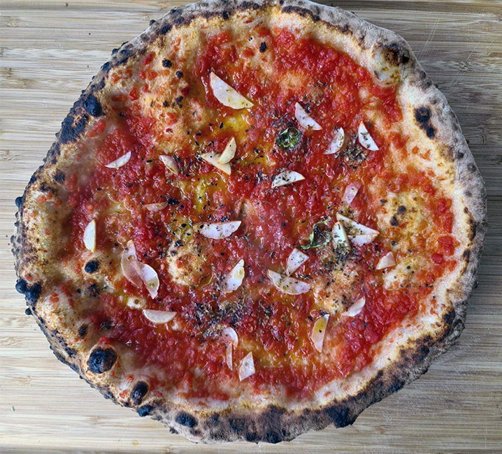 Marinara pizza topped with tomato sauce, slivers of garlic and oregano on a wooden table