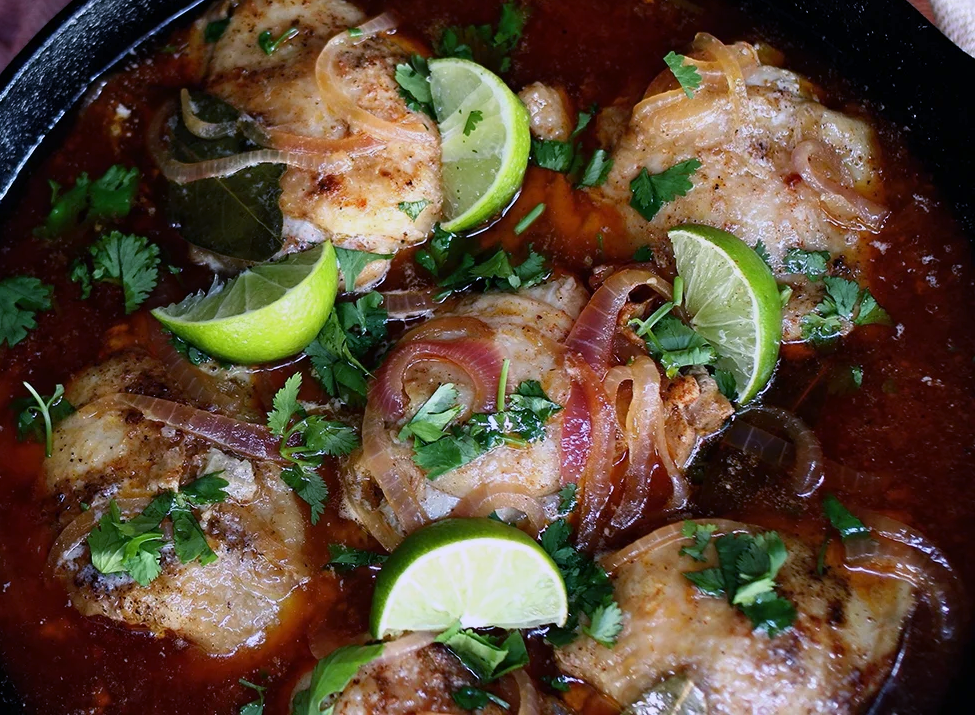 Salvadorean pollo encebollado in a cast iron pan garnished with lime wedges