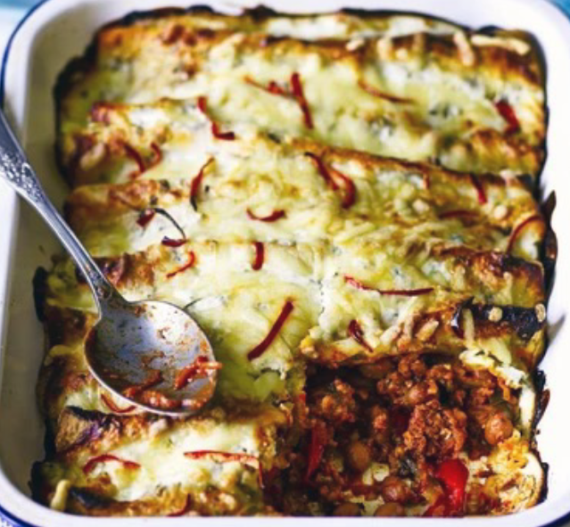 pork and chorizo enchiladas packed into a baking dish with a cheese and fromage frais topping with one corner removed to reveal the filling