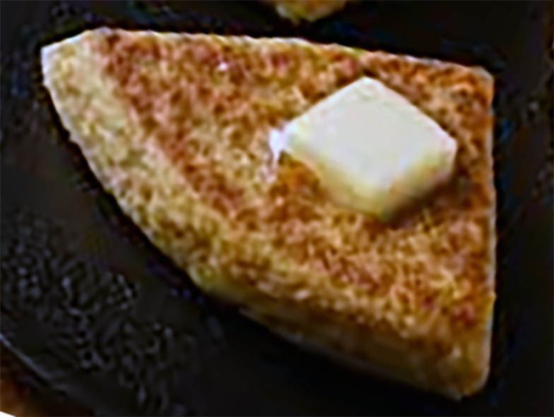 wedge of pratie oaten topped with butter frying on a griddle pan