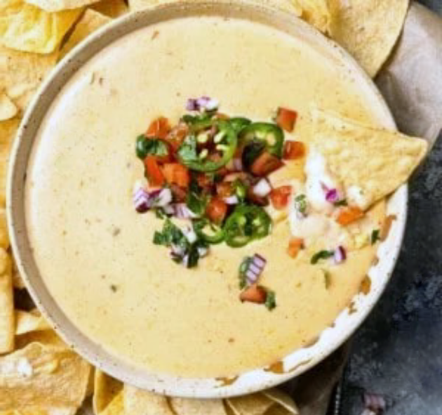 white queso cheese dip in a bowl with a garnish of pico de gallo and jalapeno chillies surrounded by tortilla chips