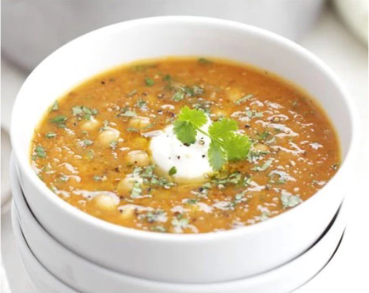 red lentil chickpea and chilli soup served in a white bowl with a garnish of greek yoghurt and a coriander sprig