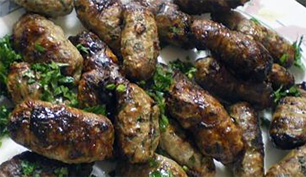 fried sheftalia sausages piled on a plate and garnished with parsley