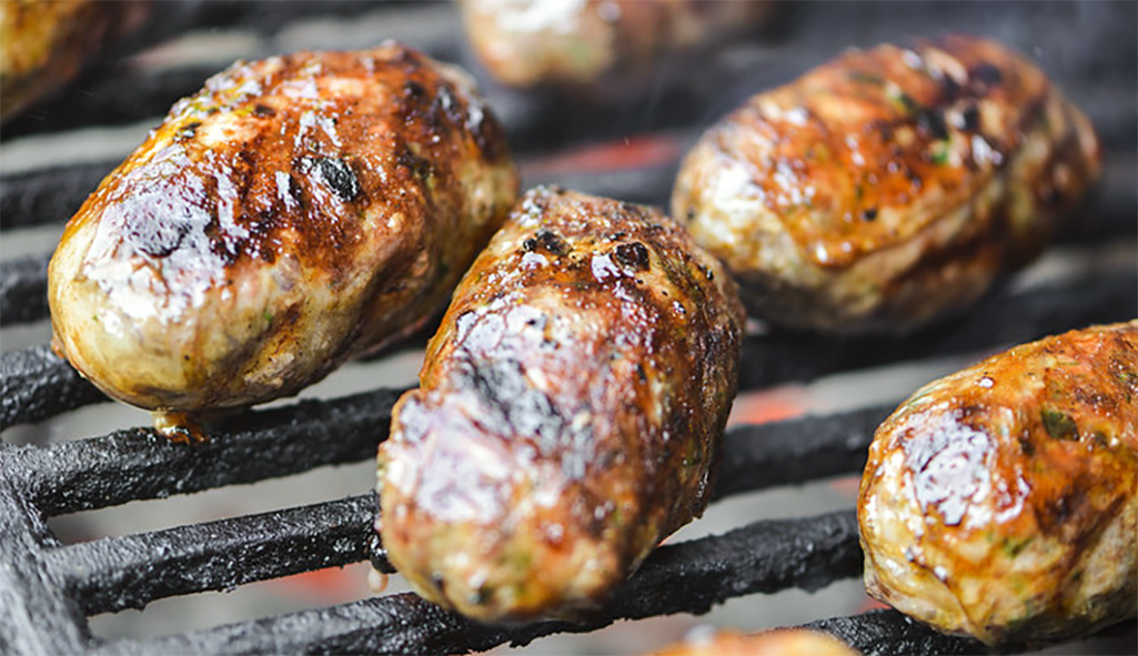 sieftalia, caul-wrapped sausages cooking on a barbecue
