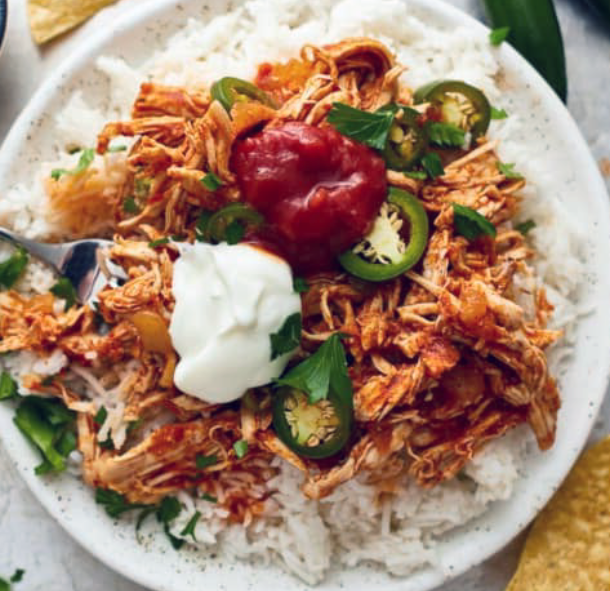 chicken cooked in a slow cooker using a salsa base served on a bed of rice with a garnish of jalapenos, sour cream and tomato sauce