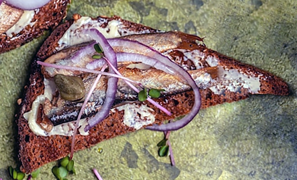 open sandwich of smoked sprats with mustard sauce on rye bread topped with red onion