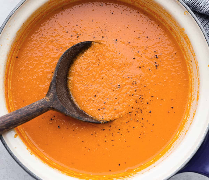 tomato and lettuce soup in an enamelled pot with a wooden spoon