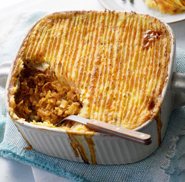vegetarian lentil cottage pie in a white ceramic baking dish with the bottom left corner removed to reveal the filling