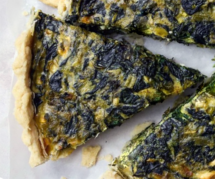 wedge of spinach tart on a sheet of baking paper