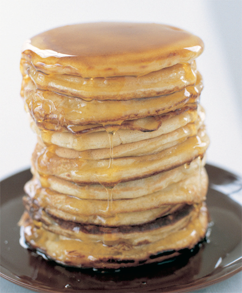 tall stack of American style breakfast pancakes drizzled with maple syrup