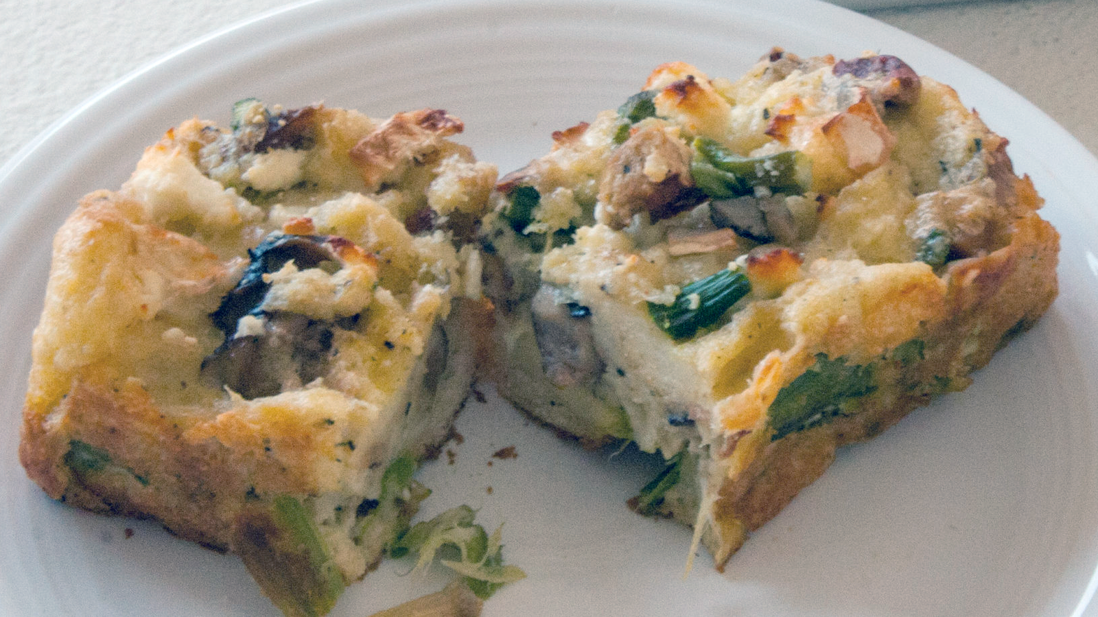two pieces of asparagus and morel bread pudding on a white plate