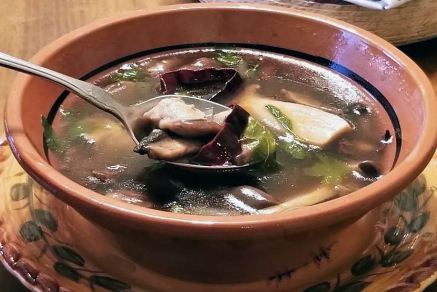 clear Mexican mushroom soup served in an earthenware bowl with a spoon
