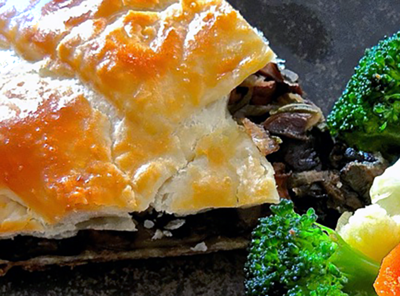 slice of chanterelle and spinach pie shown with broccoli, carrot and cauliflower