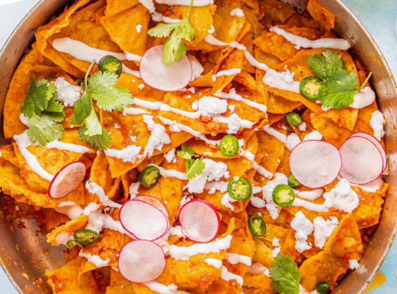 chilaquiles of tortilla chips simmered in salsa served topped with coriander, radish and Mexican crema