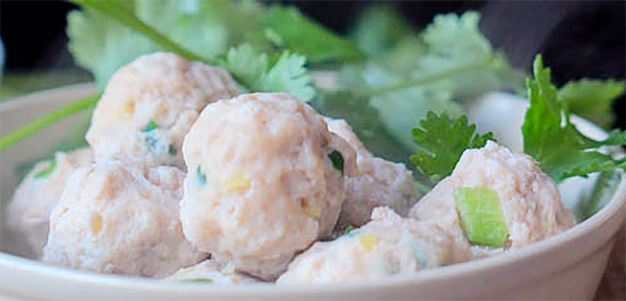 Sichuan style pork meatballs piled in a white bowl with a garnish of spring onion leaves