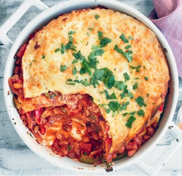 enchilada pie topped with tortilla, sour cream and cheese with a spoonful removed to reveal the filling
