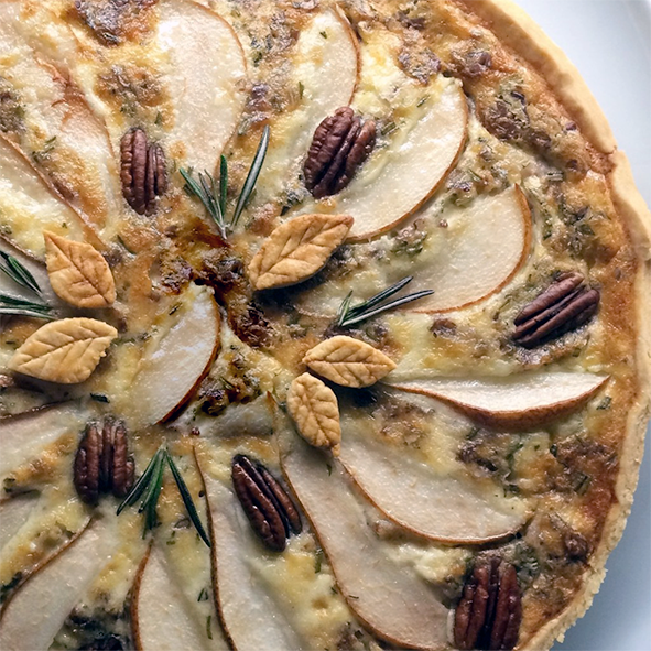 pear, goat cheese and walnut/pecan nut quiche viewed from above with a garnish of pastry leaves and rosemary