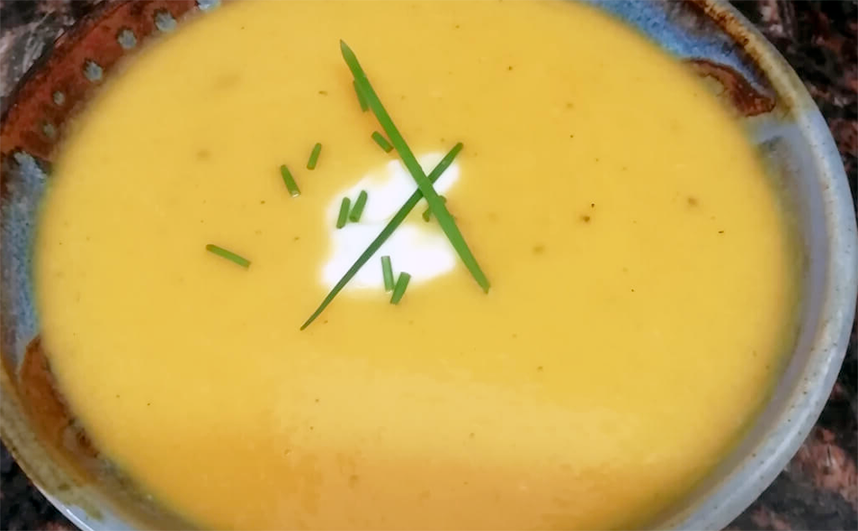 golden vegetable soup served in a bowl with a garnish of sour cream and snipped chives