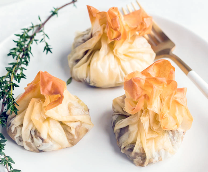 filo parcels with hedgehog fungus in a tomato sauce filling on a plate with a fork and a sprig of thyme